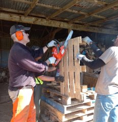 A volunteer using a chainsaw to cut up a wood pallet.