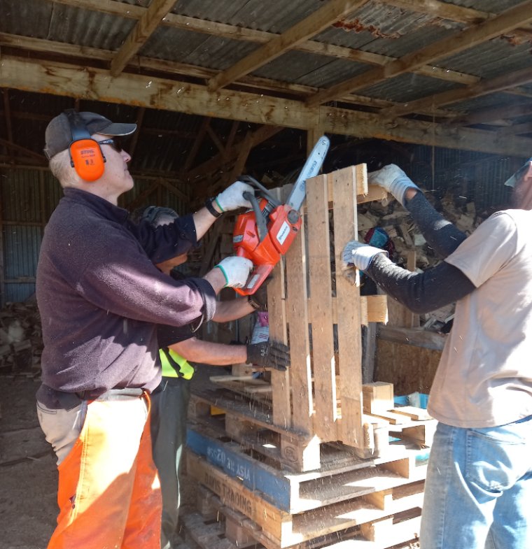 A volunteer using a chainsaw to cut up a wood pallet.
