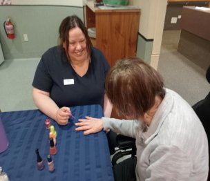 Bex sat smiling with a resident as she paints their nails.