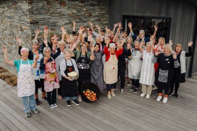Group photo of Food For Love volunteers with their hands in the air, some holding up produce, smiling at the camera