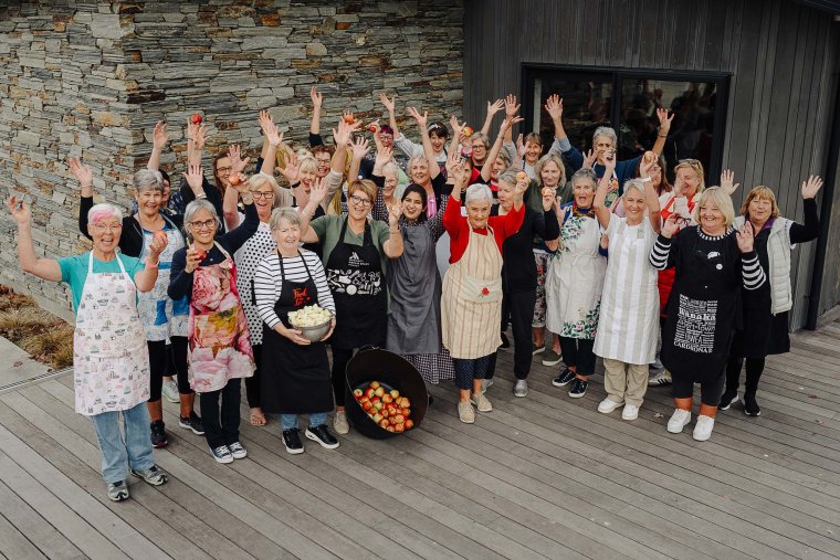 Group photo of Food For Love volunteers with their hands in the air, some holding up produce, smiling at the camera