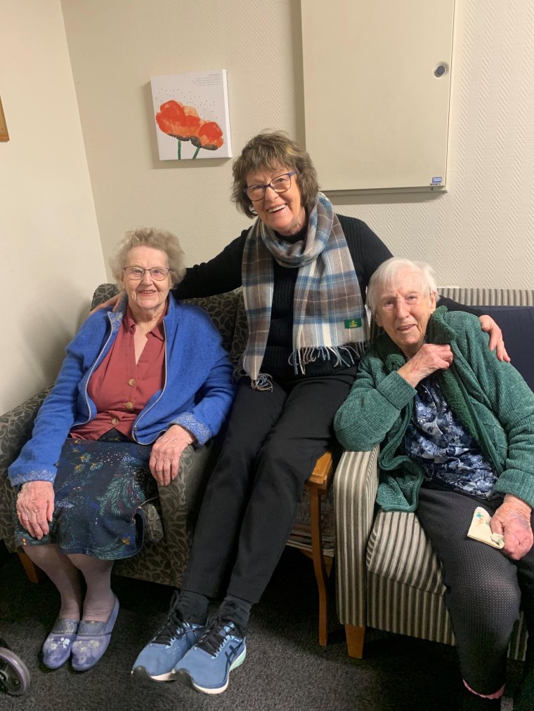 Gloria Todd sat with her arms around two elderly residents sat on  armchairs, all smiling at the camera