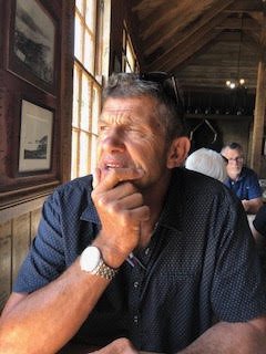 A head and shoulder photo of Trevor sitting a table looking out a window