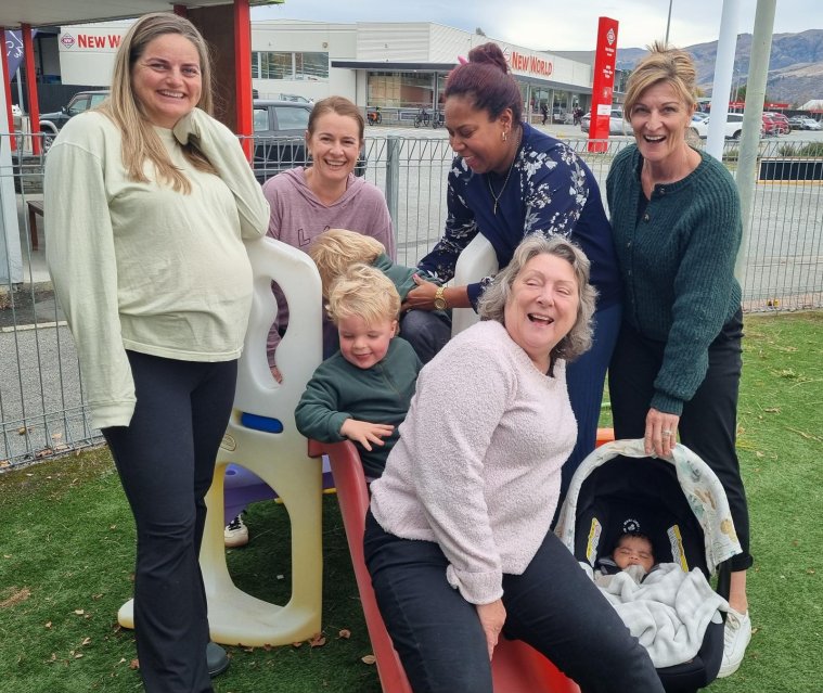 Group of woman and a baby in a car seat in a childrens Playgroup, smiling for the camera