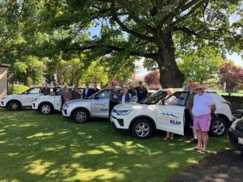 A group of CO REAP's Drive My Life Mentors standing amongst four of CO REAP's vehicles.