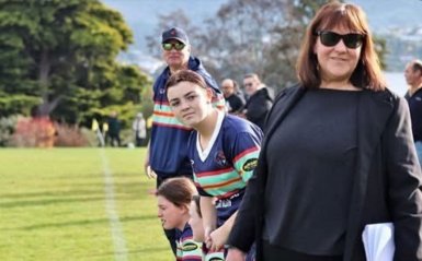 Paula stood on the sidelines of a rugby game, with a few players watching the game beside her.