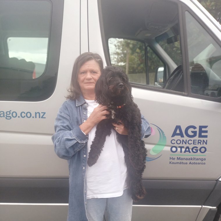 Helen holding her dog Audrey, standing in front of the Age Concern van.