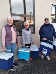 Three volunteers holding chilly bins and smiling at the camera.