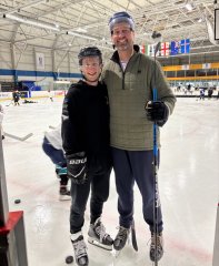 Mat and Toby in ice hockey gear on the ice, smiling at the camera.