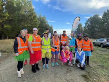 Group of volunteers in high-vis vests stood in front of a parkrun teardrop banner, smiling at the camera.