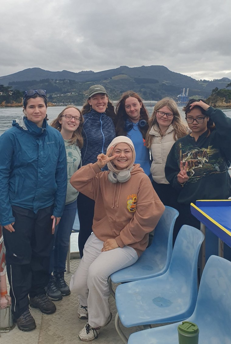 A group of student volunteers together aboard a boat, smiling at the camera.