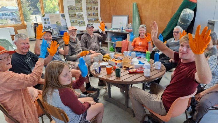Group of volunteers holdind up their colourful gloved hands and smiling at the camera.