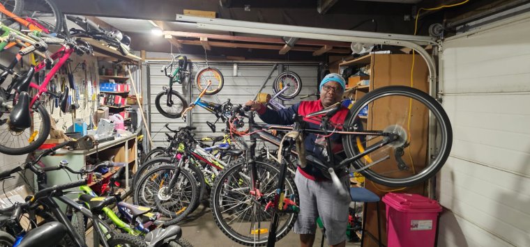 Sabelo holding up a bike, standing in a garage full of many bikes.
